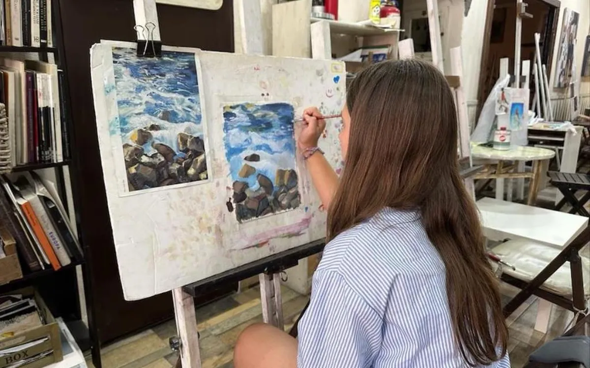 Alumna pintando un paisaje de mar en un caballete del taller