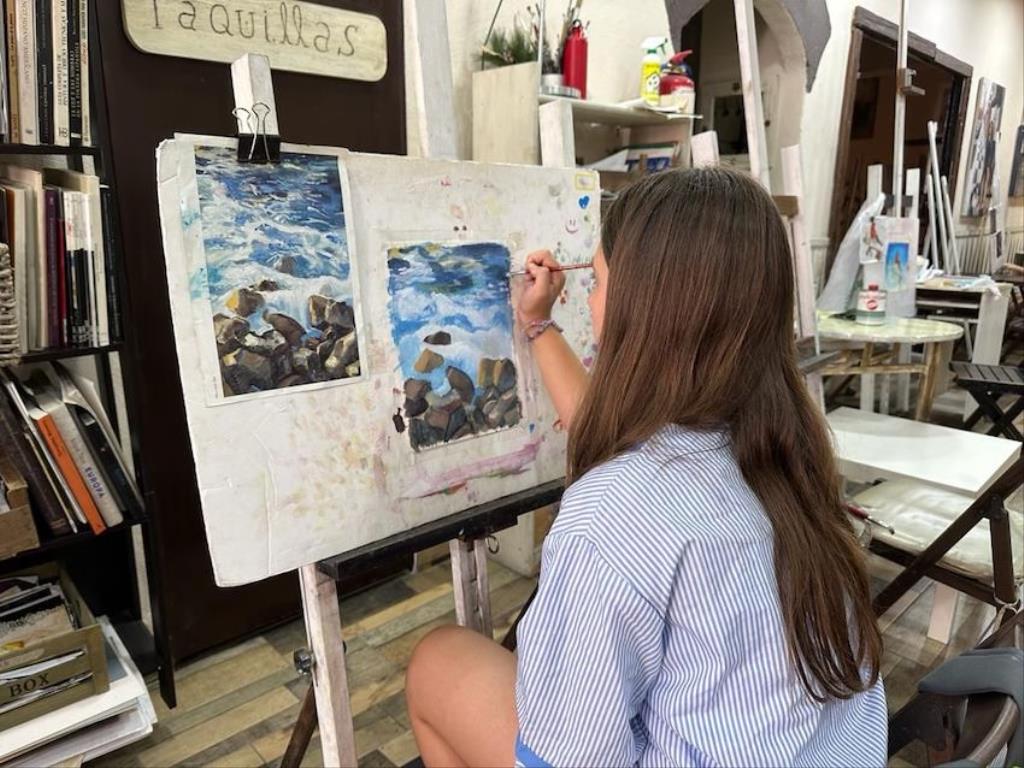 Alumna pintando un paisaje de mar en un caballete del taller