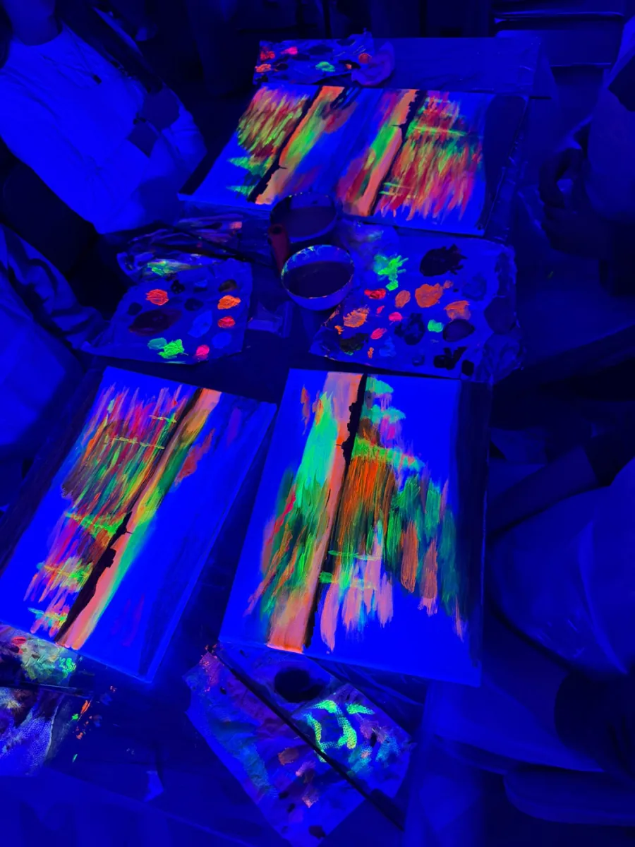 Lienzos pintados con colores neón brillando bajo luz ultravioleta en un taller de pintura con neón