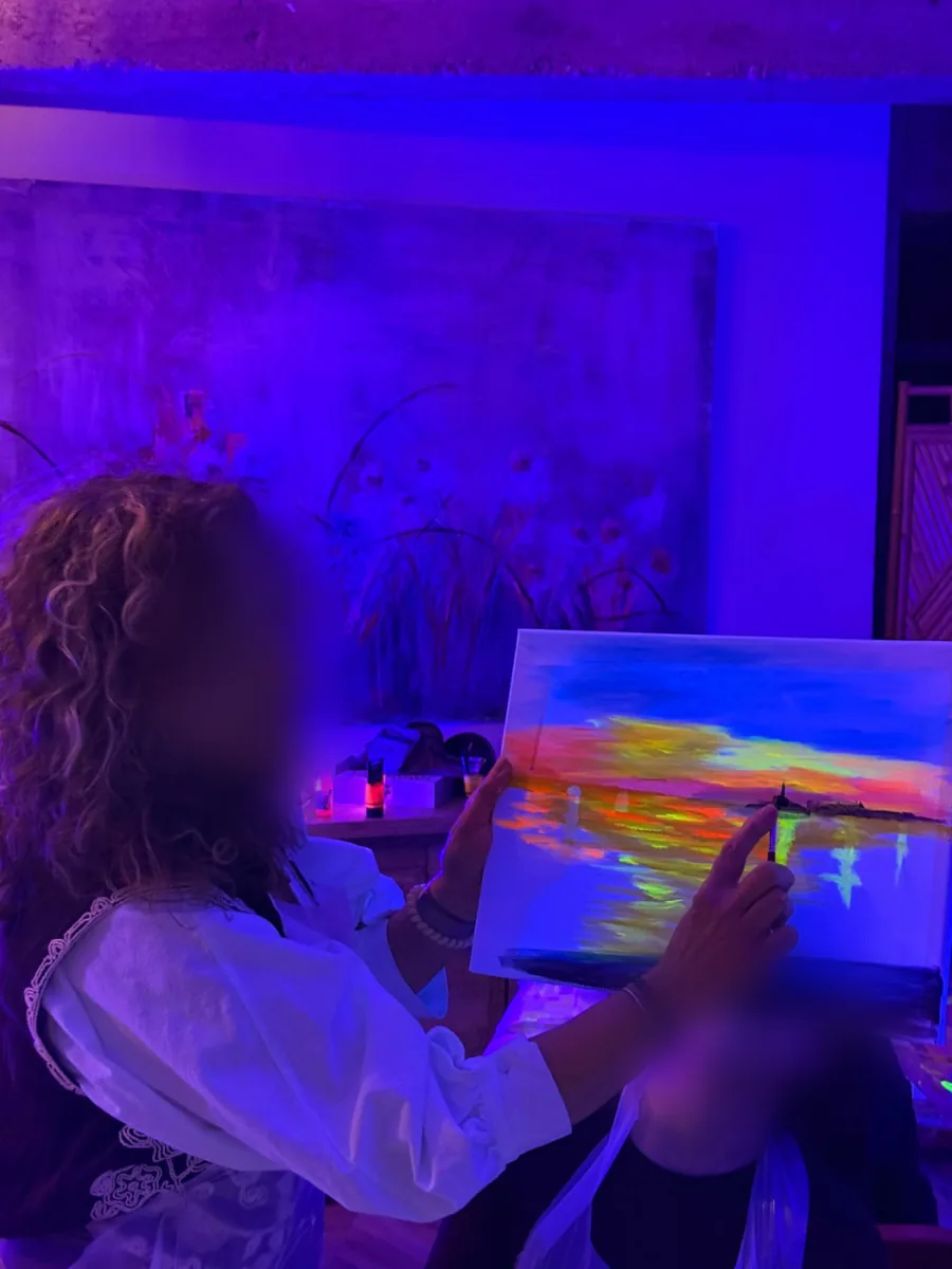 Profesora mostrando un cuadro de atardecer pintado con colores neón